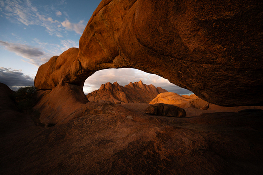 View of the rugged sun kissed archway framing distant peaks under a serene sky capturing the raw beauty of the arid landscape Spitzkoppe Erongo Region Namibia.