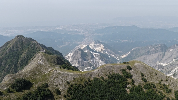 Aerial view of the famous Carrara marble quarries in the Apuan Alps showing white marble scars on the mountains rugged terrain and distant valley views in Carrara Tuscany Italy. Aerial view of the famous Carrara marble quarries in the Apuan Alps showing white marble scars on the mountains rugged terrain and distant valley views in Carrara Tuscany Italy.