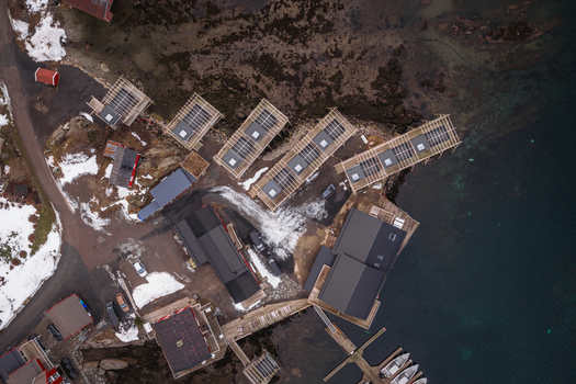 Aerial view of the fishing village where the dark buildings meet the cold dark waters with patches of snow clinging to the rocky shores Ballstad Nordland Norway. Aerial view of the fishing village where the dark buildings meet the cold dark waters with patches of snow clinging to the rocky shores Ballstad Nordland Norway.