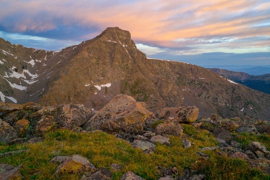 Aerial view of Mount of the Holy Cross in the Sawatch Range of the Rocky Mountains with rocky terrain and patches of snow under a dramatic sunset sky in Vail Colorado United States. Aerial view of Mount of the Holy Cross in the Sawatch Range of the Rocky Mountains with rocky terrain and patches of snow under a dramatic sunset sky in Vail Colorado United States.
