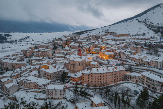Aerial view of the historic town of Rivisondoli covered in snow with traditional stone buildings a church with a red bell tower and surrounding mountains in Rivisondoli Abruzzo Italy.