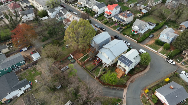 Aerial view of a residential neighborhood with houses featuring metal roofs and solar panels surrounded by trees and streets in Charlottesville Virginia United States.