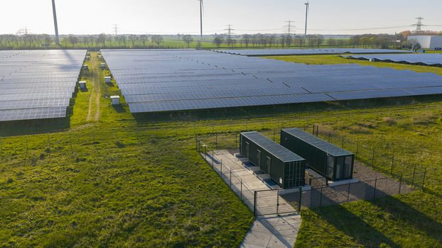 Aerial view of a large solar farm with rows of photovoltaic panels battery storage containers and wind turbines under a clear sky in Farmsum Groningen Netherlands.