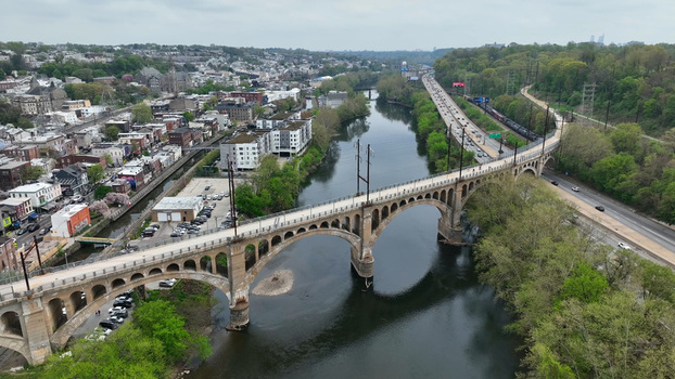Aerial view of the historic Manayunk Bridge spanning the Schuylkill River surrounded by lush green trees urban rooftops and a nearby highway in Philadelphia Pennsylvania United States.