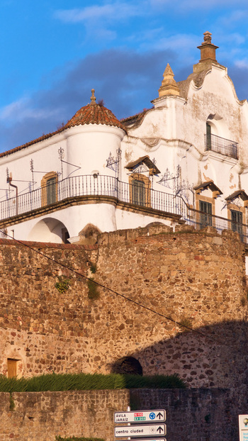 Plasencia Spain 02 December 2025 View of the historic white building with a wrought iron balcony and stone fortifications under a blue sky. Plasencia Spain 02 December 2025 View of the historic white building with a wrought iron balcony and stone fortifications under a blue sky.