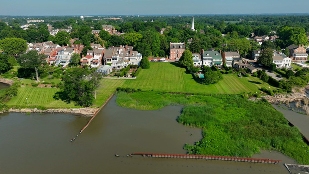 Aerial view of the historic New Castle waterfront featuring colonial style houses lush green lawns and marshy riverbanks along the Delaware River in New Castle Delaware United States.