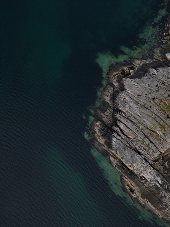 Aerial view of the rugged rocky coastline and clear turquoise water at Rorvikstranda Henningsvaer Nordland Norway.