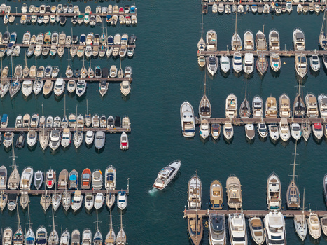Aerial view of the marina in Antibes with numerous yachts and boats docked in rows and one vessel navigating through the water in Antibes Provence Alpes Cote d Azur France. Aerial view of the marina in Antibes with numerous yachts and boats docked in rows and one vessel navigating through the water in Antibes Provence Alpes Cote d Azur France.