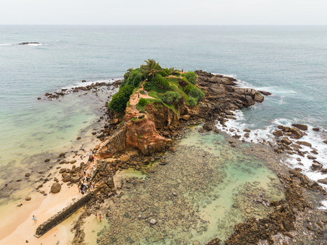 Aerial view of Parrot Rock with people walking along the narrow path surrounded by turquoise ocean and coral reefs in Mirissa Southern Province Sri Lanka. Aerial view of Parrot Rock with people walking along the narrow path surrounded by turquoise ocean and coral reefs in Mirissa Southern Province Sri Lanka.
