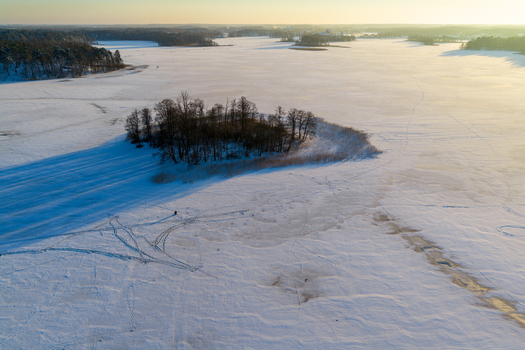 Aerial view of a small island with bare trees on a frozen snow covered lake during sunset Lithuania. Aerial view of a small island with bare trees on a frozen snow covered lake during sunset Lithuania.