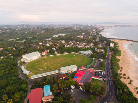 Aerial view of a green sports field surrounded by tropical trees and urban buildings along the coastline in Galle Southern Province Sri Lanka.