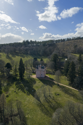 Aerial view of Craigievar Castle with its iconic pink walls surrounded by lush green fields and dense forests under a bright blue sky Craigievar Scotland United Kingdom.
