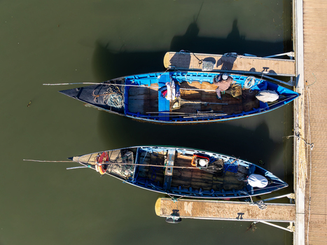 Aerial view of vibrant blue boats moored beside a concrete pier casting shadows on the still dark water Porta de Abrigo da Torreira Aveiro Portugal. Aerial view of vibrant blue boats moored beside a concrete pier casting shadows on the still dark water Porta de Abrigo da Torreira Aveiro Portugal.