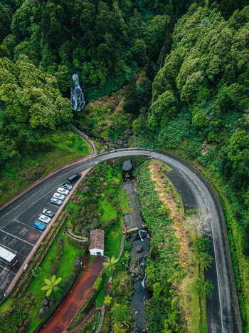 Aerial view of a winding road curves gracefully through vibrant greenery leading to a stone bridge and a cascading waterfall Achada Açores Portugal. Aerial view of a winding road curves gracefully through vibrant greenery leading to a stone bridge and a cascading waterfall Achada Açores Portugal.