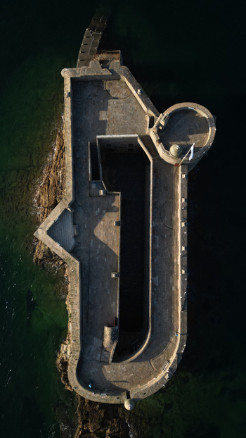 Aerial view of Chateau du Taureau a formidable stone fortress its grey walls contrasting with dark emerald waters and jagged rocks Plouezoc h Bretagne France. Aerial view of Chateau du Taureau a formidable stone fortress its grey walls contrasting with dark emerald waters and jagged rocks Plouezoc h Bretagne France.