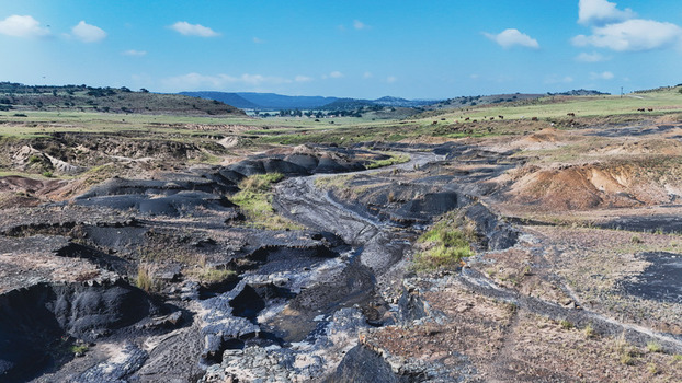 Aerial view of the rugged landscape with dark eroded soil and a winding gully under a blue sky in Pietermaritzburg KwaZulu Natal South Africa.