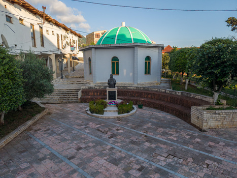 Aerial view of the green domed Bektashi Tekke and a memorial statue in a paved square surrounded by historic buildings and lush trees in Kruje Durres County Albania.