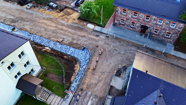 Aerial view of a construction site featuring a newly paved sidewalk road work with traffic cones and surrounding buildings in Latvija. Aerial view of a construction site featuring a newly paved sidewalk road work with traffic cones and surrounding buildings in Latvija.