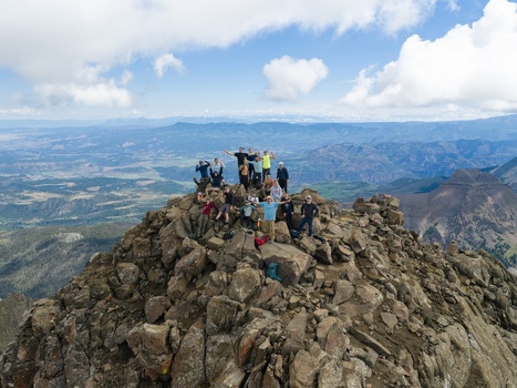 Aerial view of a group of hikers standing on the rocky summit of Mount Sneffels in the San Juan Mountains surrounded by a vast mountain landscape in Ouray County Colorado United States. Aerial view of a group of hikers standing on the rocky summit of Mount Sneffels in the San Juan Mountains surrounded by a vast mountain landscape in Ouray County Colorado United States.