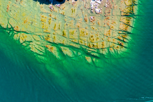 Aerial view of Lake Garda s rocky shoreline with people sunbathing on flat stone slabs and turquoise water in Italy. Aerial view of Lake Garda s rocky shoreline with people sunbathing on flat stone slabs and turquoise water in Italy.