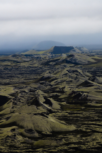 View of a mossy lava field stretches under a cloudy sky with distant mountains fading into the horizon in Skaftárhreppur Iceland. View of a mossy lava field stretches under a cloudy sky with distant mountains fading into the horizon in Skaftárhreppur Iceland.