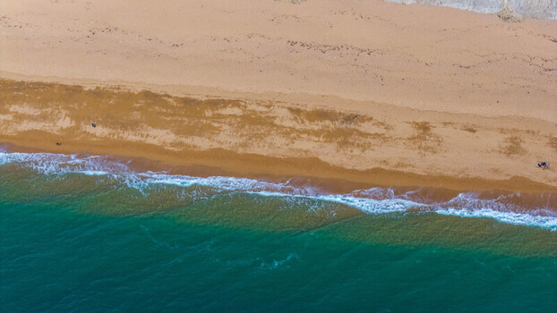 Aerial view of the sandy beach and turquoise waters at West Bay with gentle waves washing onto the shore in West Bay England United Kingdom. Aerial view of the sandy beach and turquoise waters at West Bay with gentle waves washing onto the shore in West Bay England United Kingdom.