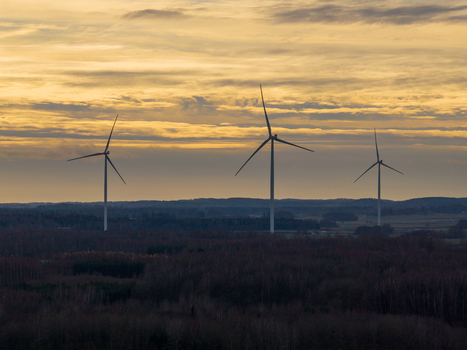 Aerial view of three wind turbines rising above a dense forest landscape under a golden sunset sky in Nemencine Vilnius County Lithuania. Aerial view of three wind turbines rising above a dense forest landscape under a golden sunset sky in Nemencine Vilnius County Lithuania.