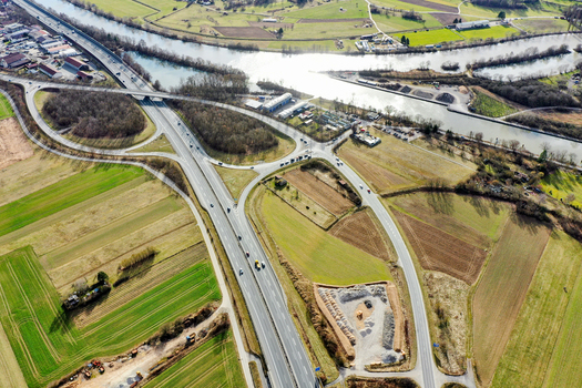 Aerial view of a highway interchange and bridge crossing a river surrounded by green fields and industrial buildings in Buttenheim Bavaria Germany. Aerial view of a highway interchange and bridge crossing a river surrounded by green fields and industrial buildings in Buttenheim Bavaria Germany.