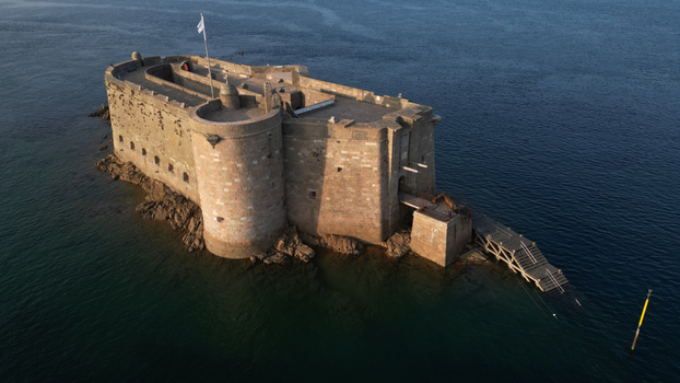Aerial view of Fort du Taureau standing steadfast against the relentless sea its ancient stone walls reflecting the golden light of the setting sun Plouezoc h Bretagne France.