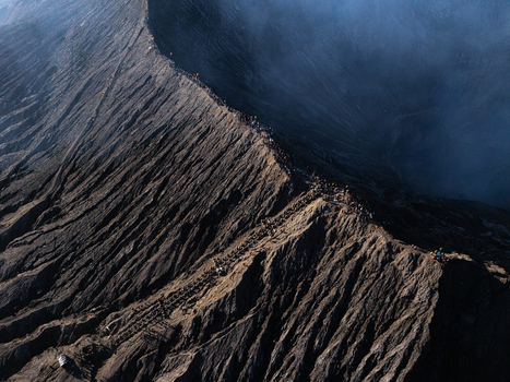 Aerial view of the rugged volcanic crater rim of Mount Bromo with people walking along the narrow ridge and dramatic shadows in Kecamatan Sukapura Jawa Timur Indonesia.