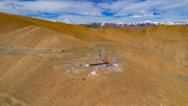Aerial view of Gawula pass featuring winding mountain roads colorful prayer flags and distant snow capped Himalayan peaks under a clear blue sky in Shigatse Tibet China.
