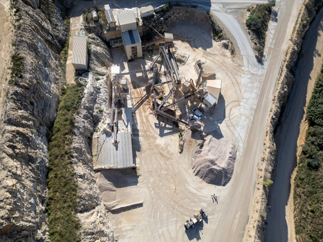 Aerial view of an industrial stone quarry featuring heavy machinery conveyor belts piles of gravel and rocky cliff faces in Teulada Valencian Community Spain.
