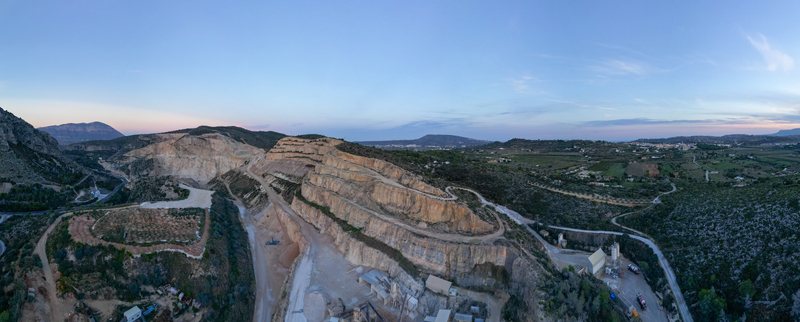 Aerial view of the quarry with terraced stone walls winding access roads and industrial facilities surrounded by hills in Teulada Valencian Community Spain.