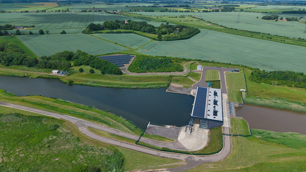 Aerial view of St Germans Pumping Station with solar panels on the roof and a nearby solar farm situated along the river and green fields in King s Lynn England United Kingdom.