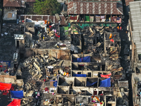 Aerial view of the fire damaged Korail Basti settlement with charred structures debris and people navigating the ruins in Dhaka Dhaka Division Bangladesh.