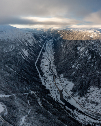 Aerial view of the snow covered town of Rjukan nestled in a deep valley surrounded by steep mountains under a cloudy sky Rjukan Telemark Norway. Aerial view of the snow covered town of Rjukan nestled in a deep valley surrounded by steep mountains under a cloudy sky Rjukan Telemark Norway.