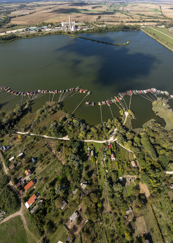 Aerial view of the Bokodi Floating Village with its iconic wooden houses on stilts extending into the lake surrounded by lush greenery and agricultural fields near Oroszlany Hungary. Aerial view of the Bokodi Floating Village with its iconic wooden houses on stilts extending into the lake surrounded by lush greenery and agricultural fields near Oroszlany Hungary.
