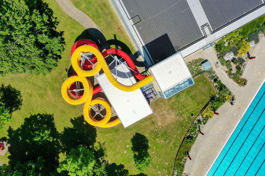 Aerial view of Konigsbad Forchheim featuring colorful red and yellow water slides lush green lawns and swimming pool facilities in Forchheim Bayern Germany. Aerial view of Konigsbad Forchheim featuring colorful red and yellow water slides lush green lawns and swimming pool facilities in Forchheim Bayern Germany.