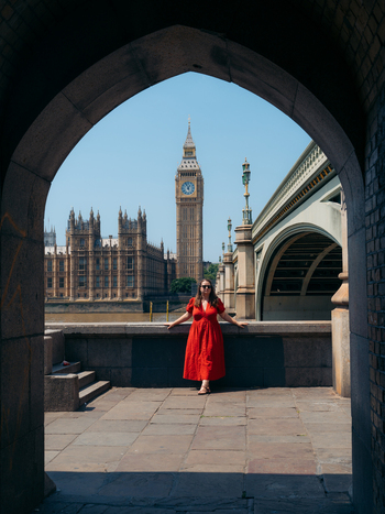 View of a woman in a striking red dress framed by a stone arch overlooking Big Ben and Parliament London England United Kingdom. View of a woman in a striking red dress framed by a stone arch overlooking Big Ben and Parliament London England United Kingdom.