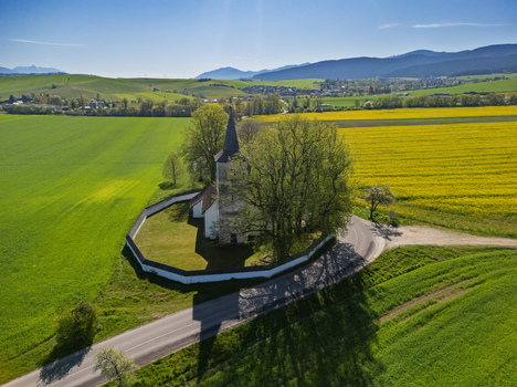 Aerial view of the historic Church of All Saints surrounded by a circular stone wall and lush trees amidst vibrant green and yellow fields Ludrova Zilina Region Slovakia. Aerial view of the historic Church of All Saints surrounded by a circular stone wall and lush trees amidst vibrant green and yellow fields Ludrova Zilina Region Slovakia.