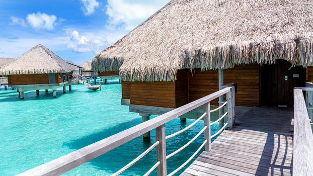 View of overwater bungalows with thatched roofs connected by wooden walkways over the turquoise lagoon in Bora Bora Leeward Islands French Polynesia.