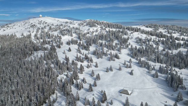 Aerial view of snow laden evergreens and a solitary structure nestled amidst the winter s embrace with a towering peak in the distance Mijoux Auvergne Rhône Alpes France. Aerial view of snow laden evergreens and a solitary structure nestled amidst the winter s embrace with a towering peak in the distance Mijoux Auvergne Rhône Alpes France.