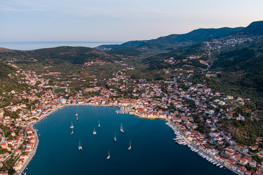 Aerial view of Ithaca town nestled in a bay with sailboats and traditional buildings surrounded by lush green hills in Ithaki Greece.