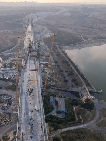 Aerial view of the construction of a large suspension bridge featuring tall yellow cranes and a concrete deck situated near a reservoir in the landscape of Istanbul Istanbul Turkiye.
