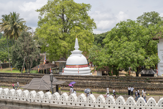 Kandy Central Province Sri Lanka 27 April 2026 View of the white stupa at Sri Dalada Maligawa surrounded by lush trees and a stone wall with people walking along the path. Kandy Central Province Sri Lanka 27 April 2026 View of the white stupa at Sri Dalada Maligawa surrounded by lush trees and a stone wall with people walking along the path.