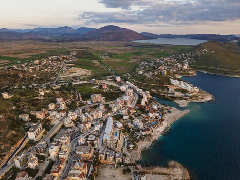 Aerial view of Saranda featuring coastal buildings residential blocks and the Ionian Sea coastline under a soft sunset sky in Saranda Vlore County Albania. Aerial view of Saranda featuring coastal buildings residential blocks and the Ionian Sea coastline under a soft sunset sky in Saranda Vlore County Albania.