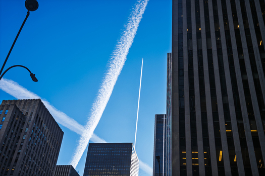Manhattan United States 03 December 2025 View of towering skyscrapers piercing a bright blue sky crisscrossed by vapor trails creating an urban tapestry of steel and sky.
