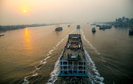 Dhaka Bangladesh 04 April 2026 Aerial view of a large ferry cutting through the murky river leaving a foamy wake under the hazy glow of the setting sun. Dhaka Bangladesh 04 April 2026 Aerial view of a large ferry cutting through the murky river leaving a foamy wake under the hazy glow of the setting sun.