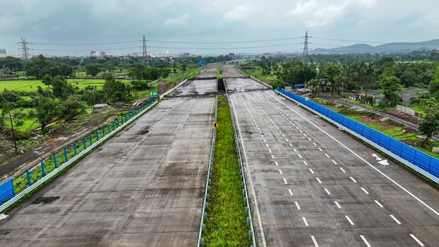 Aerial view of the Delhi Mumbai Expressway under construction with multi lane concrete road green fields and power lines in Badlapur Maharashtra India. Aerial view of the Delhi Mumbai Expressway under construction with multi lane concrete road green fields and power lines in Badlapur Maharashtra India.