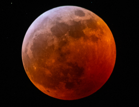 View of the moon during a total lunar eclipse with a reddish hue against the dark night sky in Canada. View of the moon during a total lunar eclipse with a reddish hue against the dark night sky in Canada.